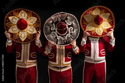 Mexican mariachi musicians cover their faces with a sombrero on a black background photo