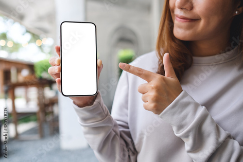 Photographie Mockup image of a young woman holding and pointing finger at a mobile phone with