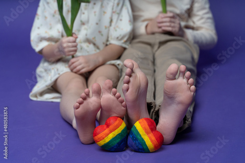 Closeup of kids' feet together with rainbow hearts. Children are sitting on the trendy very peri color background with copy space for design