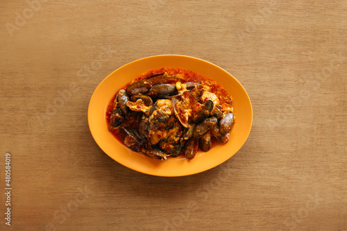 Spicy seafood sambal mussels with raw onion and chili pepper in orange plate on wood table background top view food photo