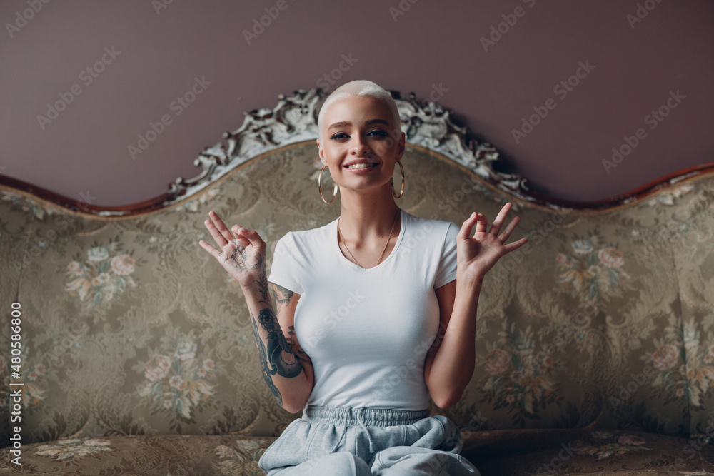 Millenial young woman with short blonde hair portrait sitting on vintage sofa.