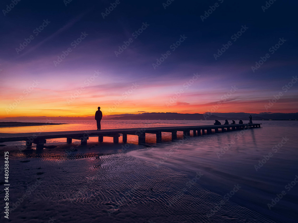 Woman from behind looking at the sunset from a pier