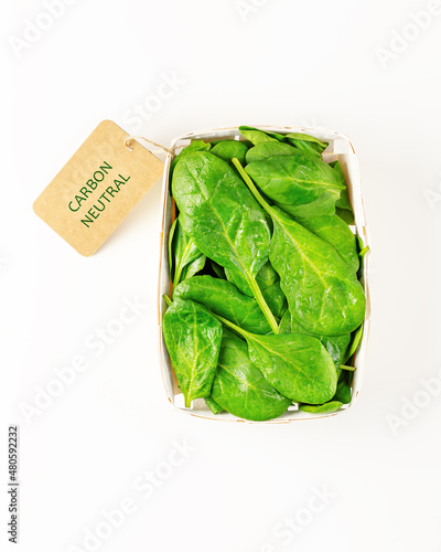 Isolated young organic spinach in an eco friendly tree bark package with a label with the inscription carbon neutral on a white background. Season lockal vegetables with carbon labeling. Flat lay photo