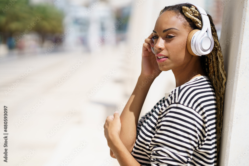 Young black woman listening to music with wireless headphones outdoors.
