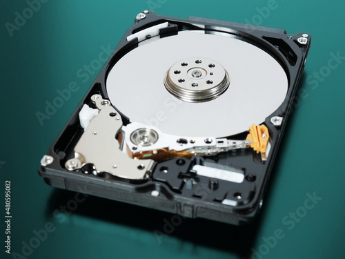 A disassembled open hard disk drive HDD of a computer or laptop lies on a turquoise matte surface.  IT&C closeup. Сomputer hardware and equipment illustration. Data storage. Macro photo