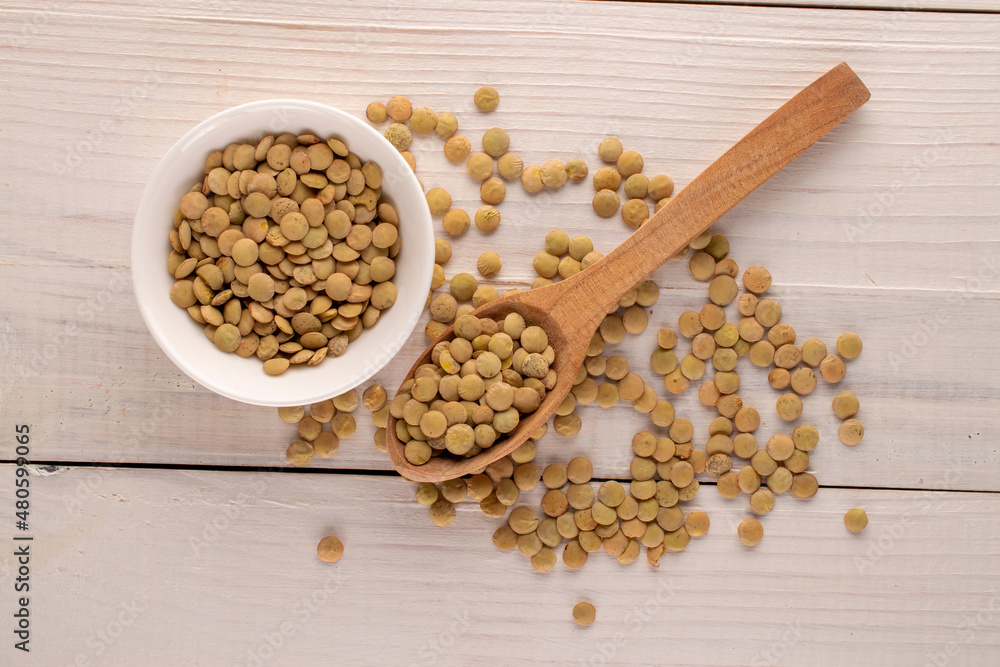 Uncooked organic green lentils with a white saucer and a wooden spoon on a wooden table, macro, top view. Uncooked organic green lentils with a white saucer and a wooden spoon on a wooden table, macro, top view.