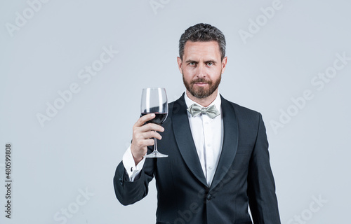 handsome tuxedo man cheers with glass of red wine hold gift box behind back, copy space, sommelier © be free