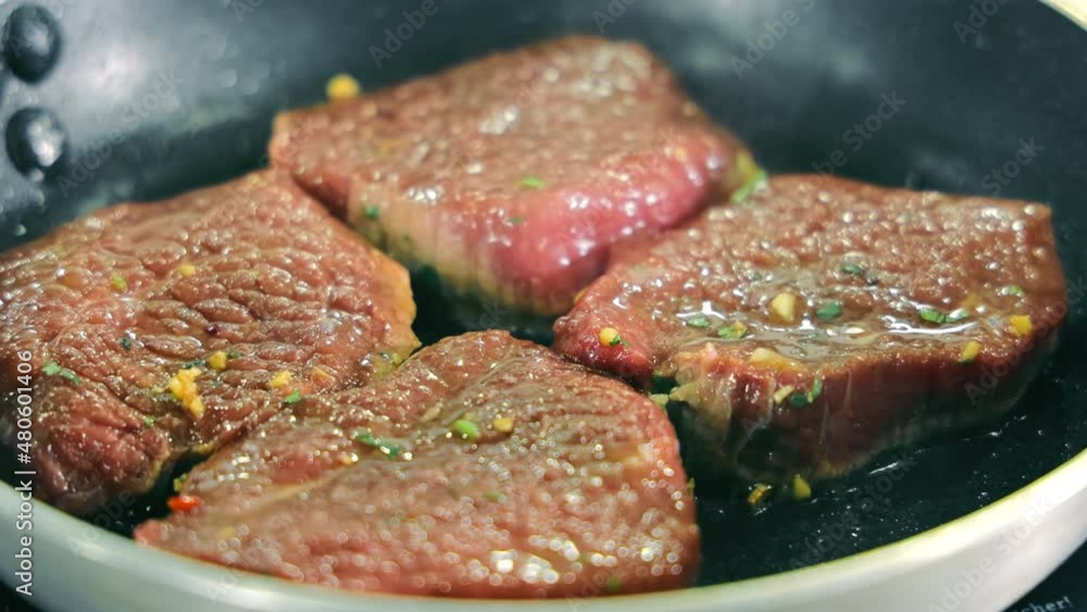 Four pieces of steak are fried in a pan. Cooking steaks at home in a pan. The chef mixes the steak pieces on the pan. Four pieces of steak are fried in a pan. Cooking steaks at home in a pan. The chef mixes the steak pieces on the pan.