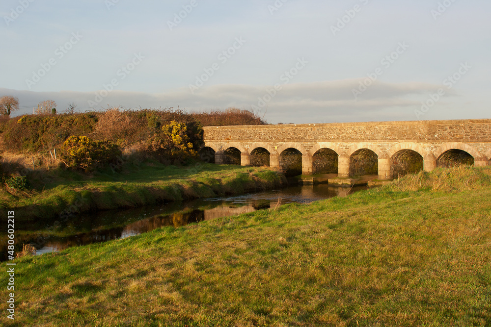 Obraz premium The soft winter sun brings out the warm glow of the sandstone used in the construction of this small 12 arches bridge at Murlough Nature Reserve near Dundrum in County Down Northern Ireland