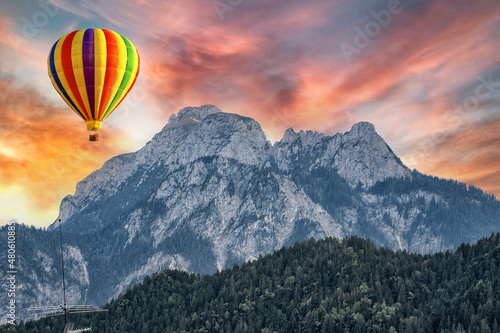 A hot air balloon on background of high Alps mountains wth green forest under bright sunset sky.