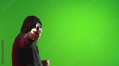 Masked man wearing a black hooded sweater carrying and pointing a gun and taunting - shot on green screen