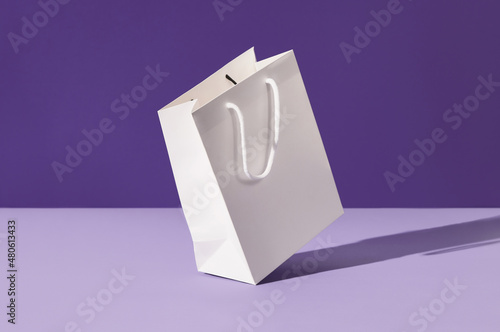 White floating paper shopping bag on purple background. Shopping sale delivery concept photo