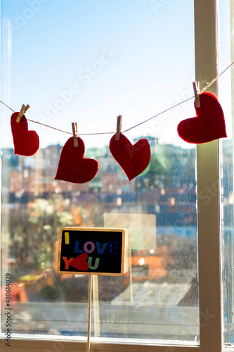 Red felt hearts hungs in window. Valentine day, romantic, love concept. View of the city photo