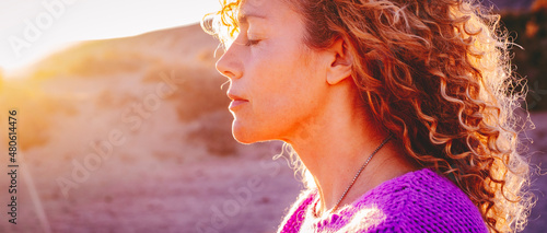 Close up sunset portrait of attractive woman with closed eyes and sun in back light. Dreaming and enjoying feeling concept lifestyle emotion. Serene female people outdoor with curly hair photo