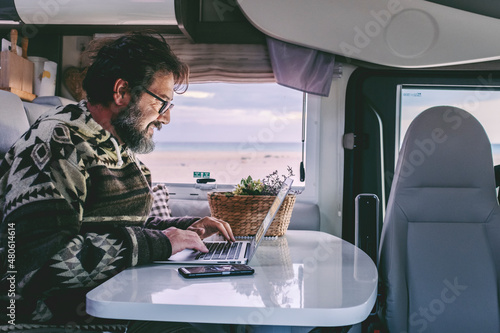 Adult man use laptop computer to work inside camper van with roaming phone connection. Concept of modern people lifestyle in smart working or travel digital nomad freedom photo