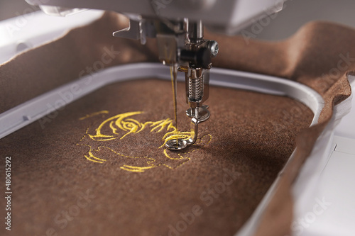 embriodery of a golden tiger head art on warm brown merino wool fabric. embroidery machine with needle, foot and hoop. selective focus