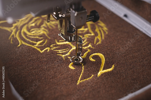 embroidery  of tiger head with number 22 graphic on brown merino wool fabric with luxurious golden yarn by modern embroidery machine. fashion and chinese new year concept. selective focus
