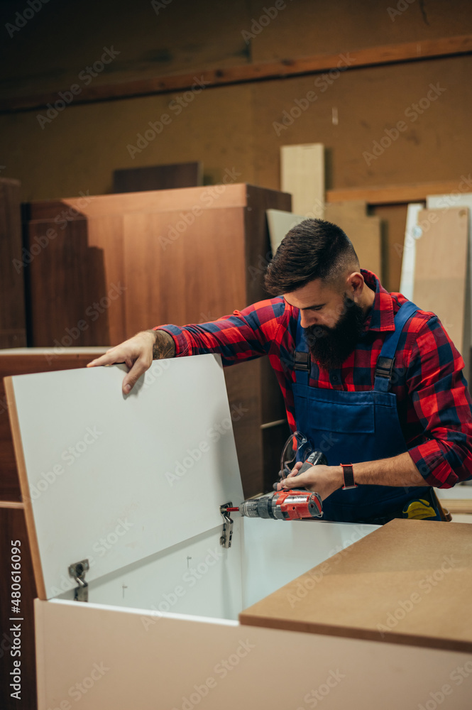 Young male carpenter working in workshop while using power drill