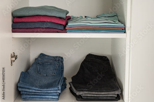 Neatly folded sweaters and jeans on shelves in wardrobe