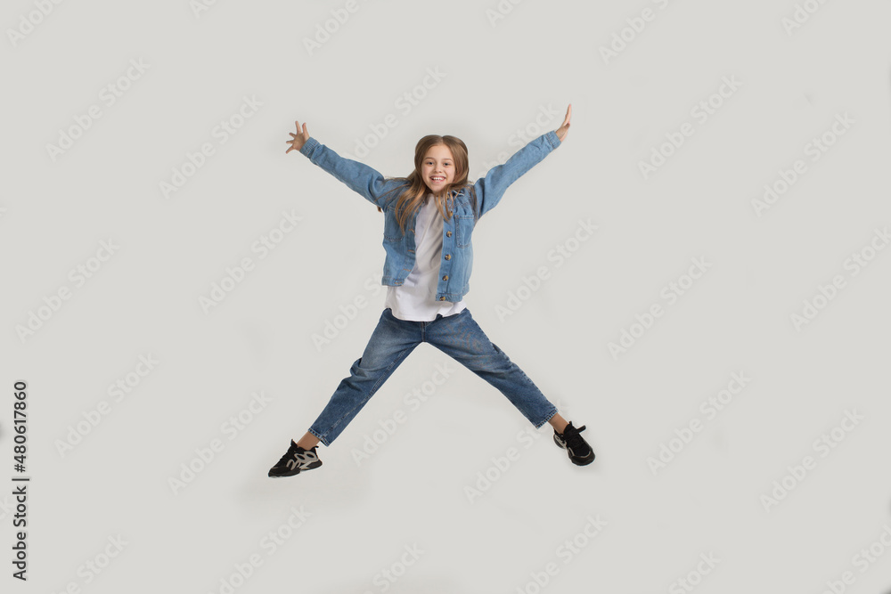 Obraz premium a young girl in jeans jumps with happiness on a white background with a copy of the space