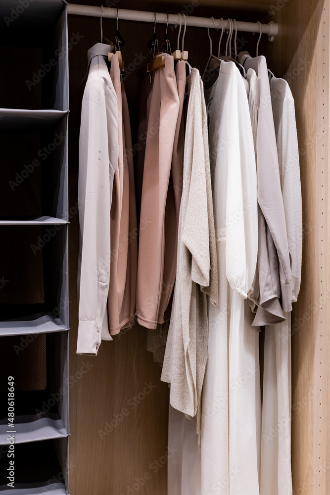 Hangers with different clothes in wardrobe closet.shirts and dress hanging on rail in wooden wardrobe at home.Clothing boutique Hangers with different clothes in wardrobe closet.shirts and dress hanging on rail in wooden wardrobe at home.Clothing boutique
