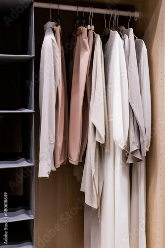 Hangers with different clothes in wardrobe closet.shirts and dress hanging on rail in wooden wardrobe at home.Clothing boutique © Yulia