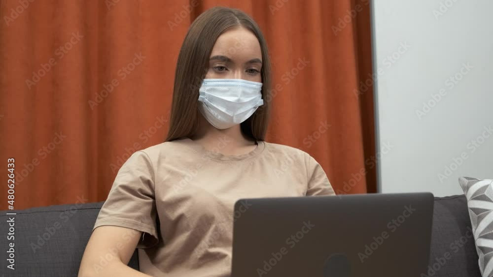 Young woman wearing face mask while working on a computer at home during virus epidemic Young woman wearing face mask while working on a computer at home during virus epidemic