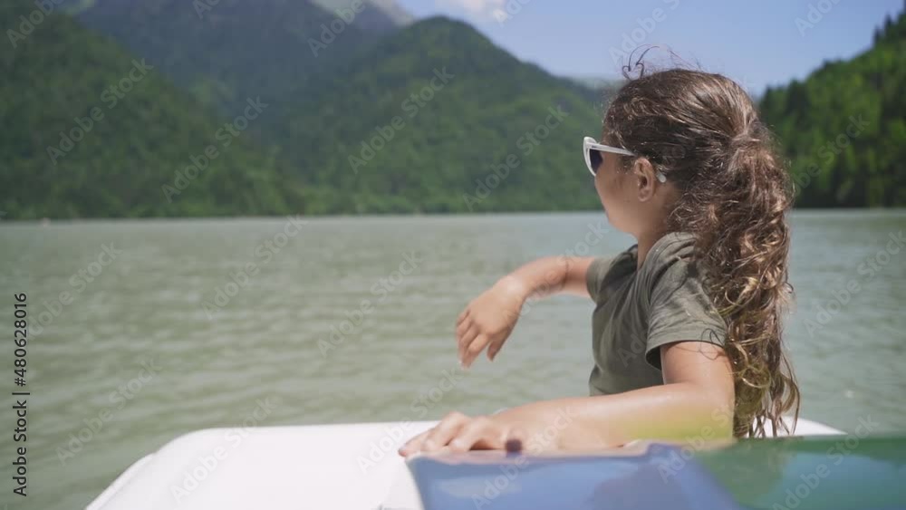 Young girl in sunglasses on catamaran sailing on mountain lake. Happy teenager resting on a boat. Family travel relaxing on water lake. Children happiness vacation on a sailboat Young girl in sunglasses on catamaran sailing on mountain lake. Happy teenager resting on a boat. Family travel relaxing on water lake. Children happiness vacation on a sailboat
