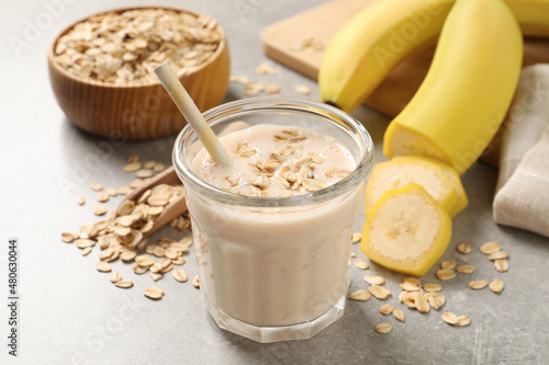 Glass of tasty banana smoothie with oatmeal on light grey table