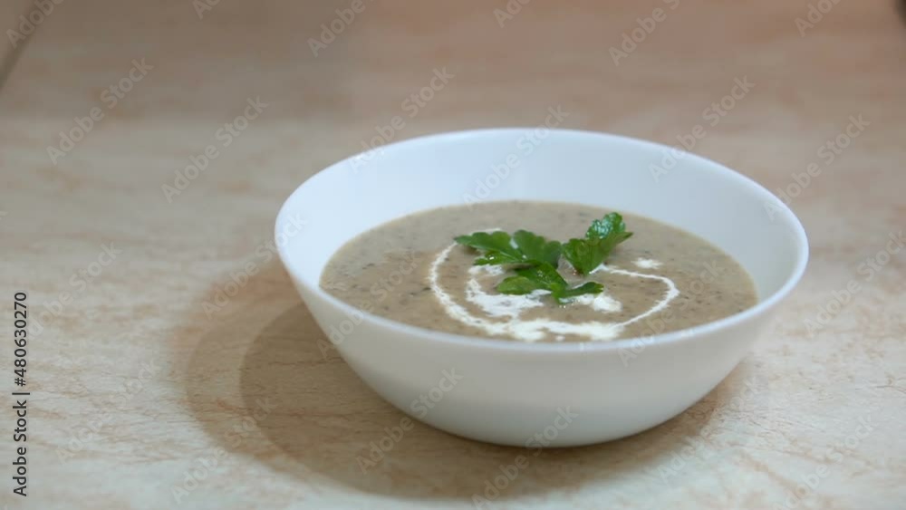 Preparation of mushroom puree soup at the kitchen, process of adding green parsley leaf to white bowl by female hands, healthy eating, nutrition concept Preparation of mushroom puree soup at the kitchen, process of adding green parsley leaf to white bowl by female hands, healthy eating, nutrition concept