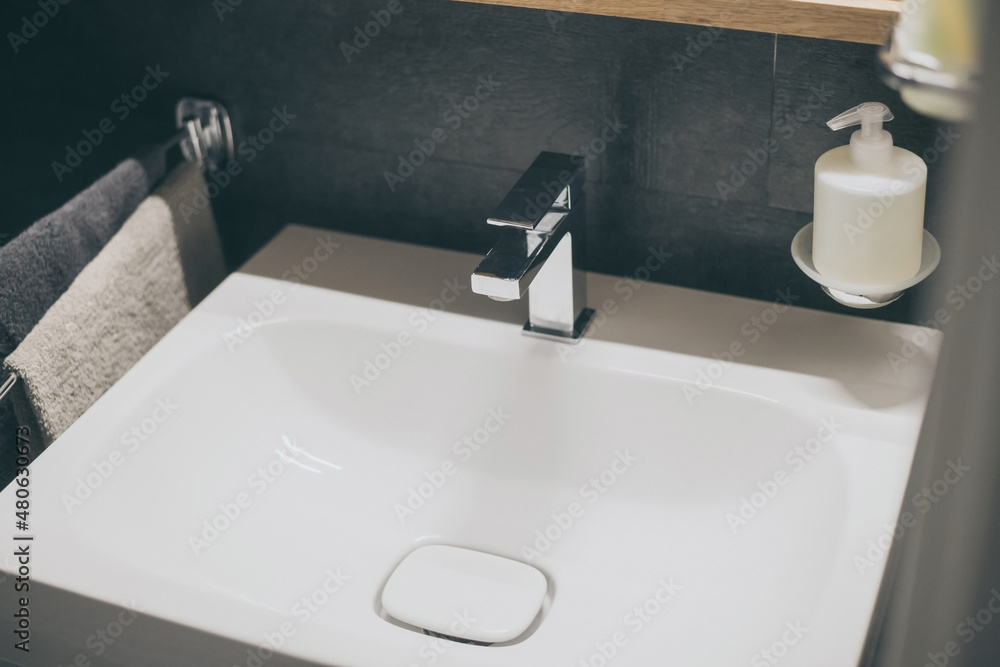 Fototapeta premium Closeup view of a sink with towels, toothbrush and soap dispenser. Modern environment bathroom fixtures with steel faucet. Cleanliness, health, recycling, pollution, cleaning, ethics, hygiene concept