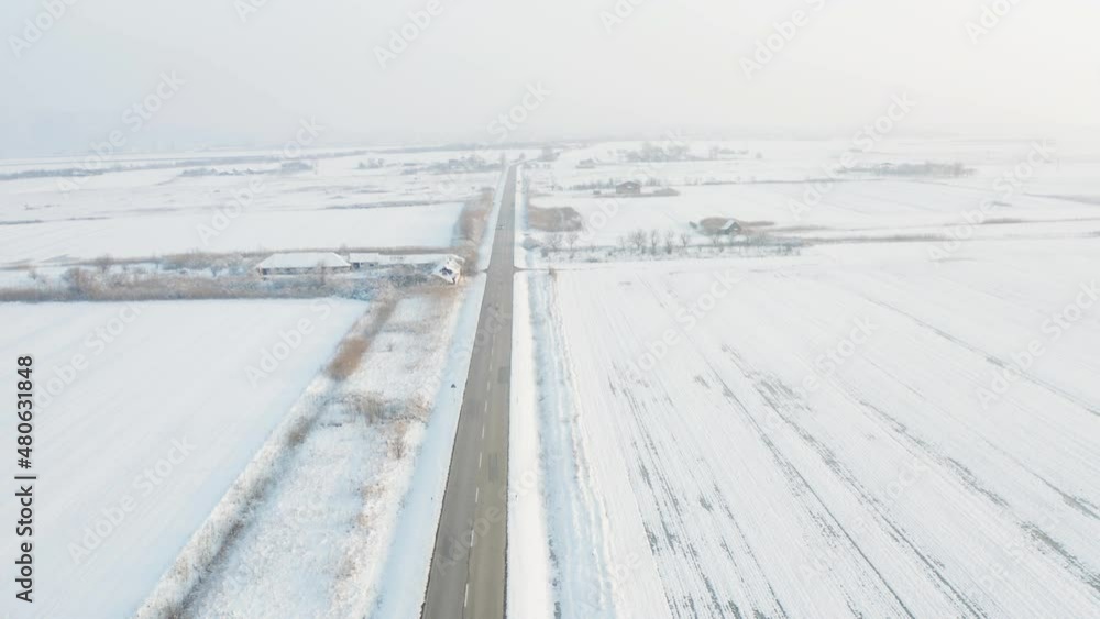 Flying high up with a camera drone above a vast wheat field covered in ice and snow with the sun setting down on the horizon making the sky bright up with some cars passing the road in the middle of a Flying high up with a camera drone above a vast wheat field covered in ice and snow with the sun setting down on the horizon making the sky bright up with some cars passing the road in the middle of a