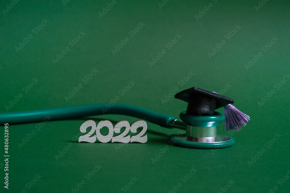 Graduation cap with stethoscope and numbers 2022 on green background, closeup with copy space. Medical education concept. Graduation cap with stethoscope and numbers 2022 on green background, closeup with copy space. Medical education concept.