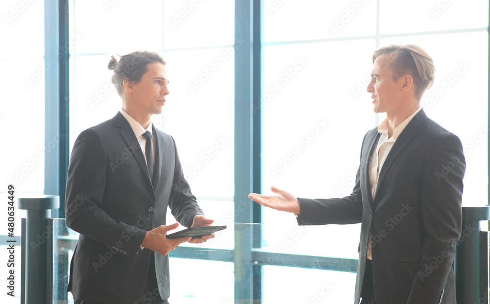two young business people working and communicating while standing at the office with city building background. two young business people working and communicating while standing at the office with city building background.