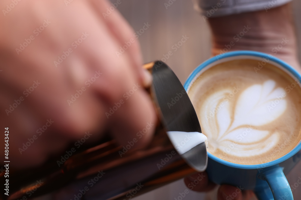 Barista pouring milk into cup of coffee, closeup