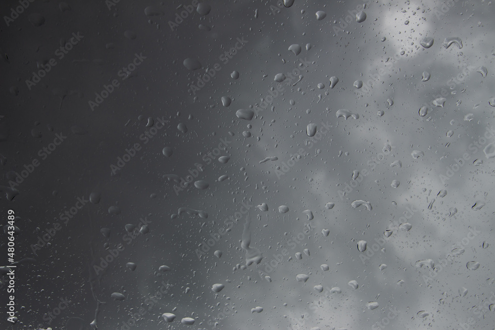 Raindrops on a window with storm clouds in the background Raindrops on a window with storm clouds in the background