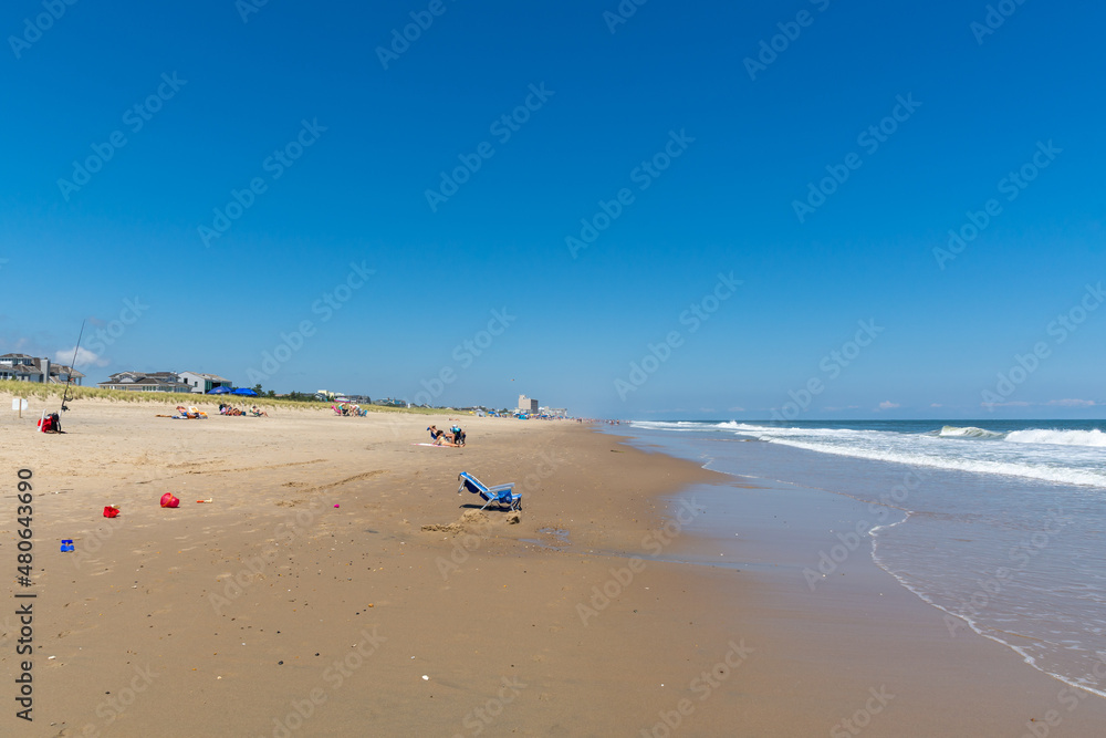 REHOBOTH, DELAWARE - USA - AUGUST 17, 2020: A relatively empty beach south of Rehoboth Beach on a sunny summer afternoon. Empty beach chair in foreground and town of Rehoboth in background.