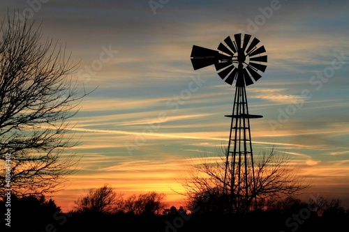 windmill at sunset that's bright and colorful with clouds and tree's north of Hutchinson Kansas USA out in the country.