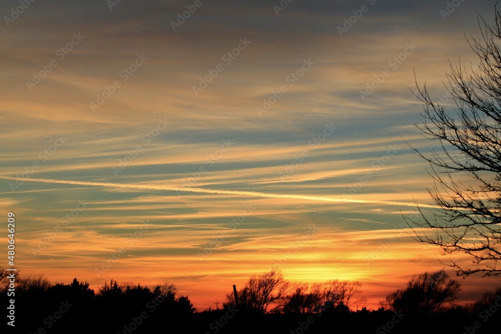 sunset over the field with colorful clouds and tree silhouettes north of Hutchinson Kansas USA out in the country.