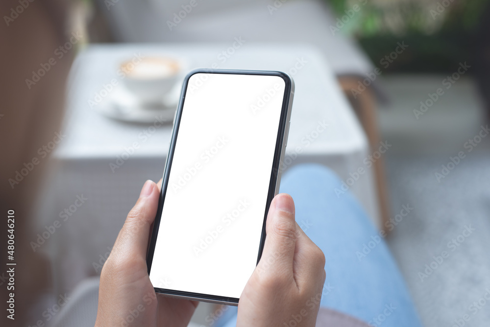 Cell phone mockup image blank white screen.  Woman hand holding, using mobile phone at coffee shop.