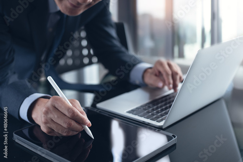 Asian businessman using stylus pen signing e-document on digital tablet with laptop computer on table at office, e-signing, electronic signature, paperless office