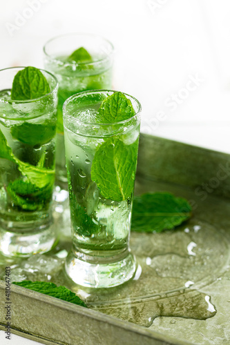 Summer Sweet Refreshing Mint Liqueur Cocktail Shots with Ice and Mint Leaves on White Wooden Background. Selective focus.