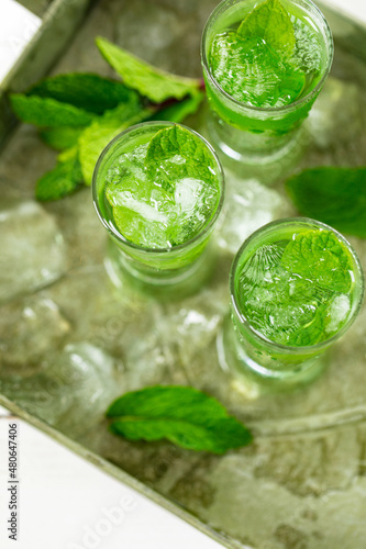 Summer Sweet Refreshing Mint Liqueur Cocktail Shots with Ice and Mint Leaves on White Wooden Background. Selective focus.