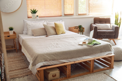 Tray with breakfast and laptop on bed in light room