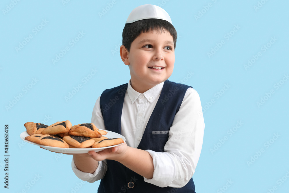 Little Jewish boy with tasty Hamantaschen for Purim holiday on color background Little Jewish boy with tasty Hamantaschen for Purim holiday on color background