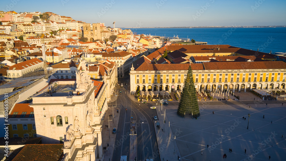Obraz premium Lisbon, Portugal - January 13, 2022: Aerial drone view of the Augusta Street Arch from Commerce Square in Lisbon, Portugal. Christmas tree in the plaza. Winter sunset.