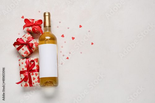 Bottle of wine and gifts for Valentine's Day on light background