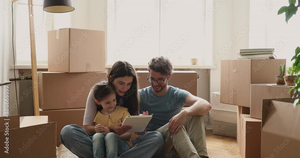 Family resting on floor on relocation day use digital tablet, buying goods, interior details on web store, search remodelling ideas online. Moving, new home, modern tech, e-commerce services concept Family resting on floor on relocation day use digital tablet, buying goods, interior details on web store, search remodelling ideas online. Moving, new home, modern tech, e-commerce services concept