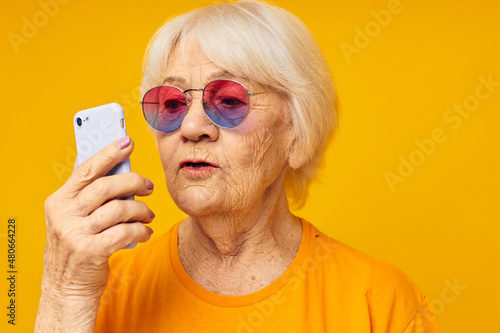 Portrait of an old friendly woman in fashionable glasses with a smartphone isolated background
