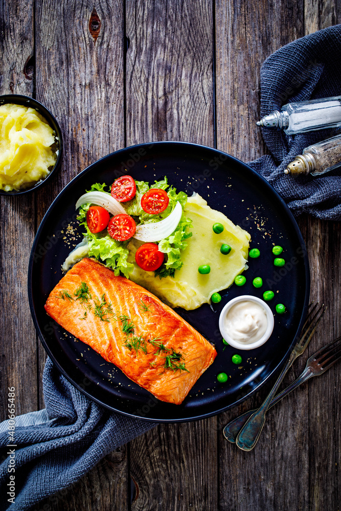 Fried salmon steak with potato puree and vegetable salad served on black plate on wooden table
Fried salmon steak with potato puree and vegetable salad served on black plate on wooden table